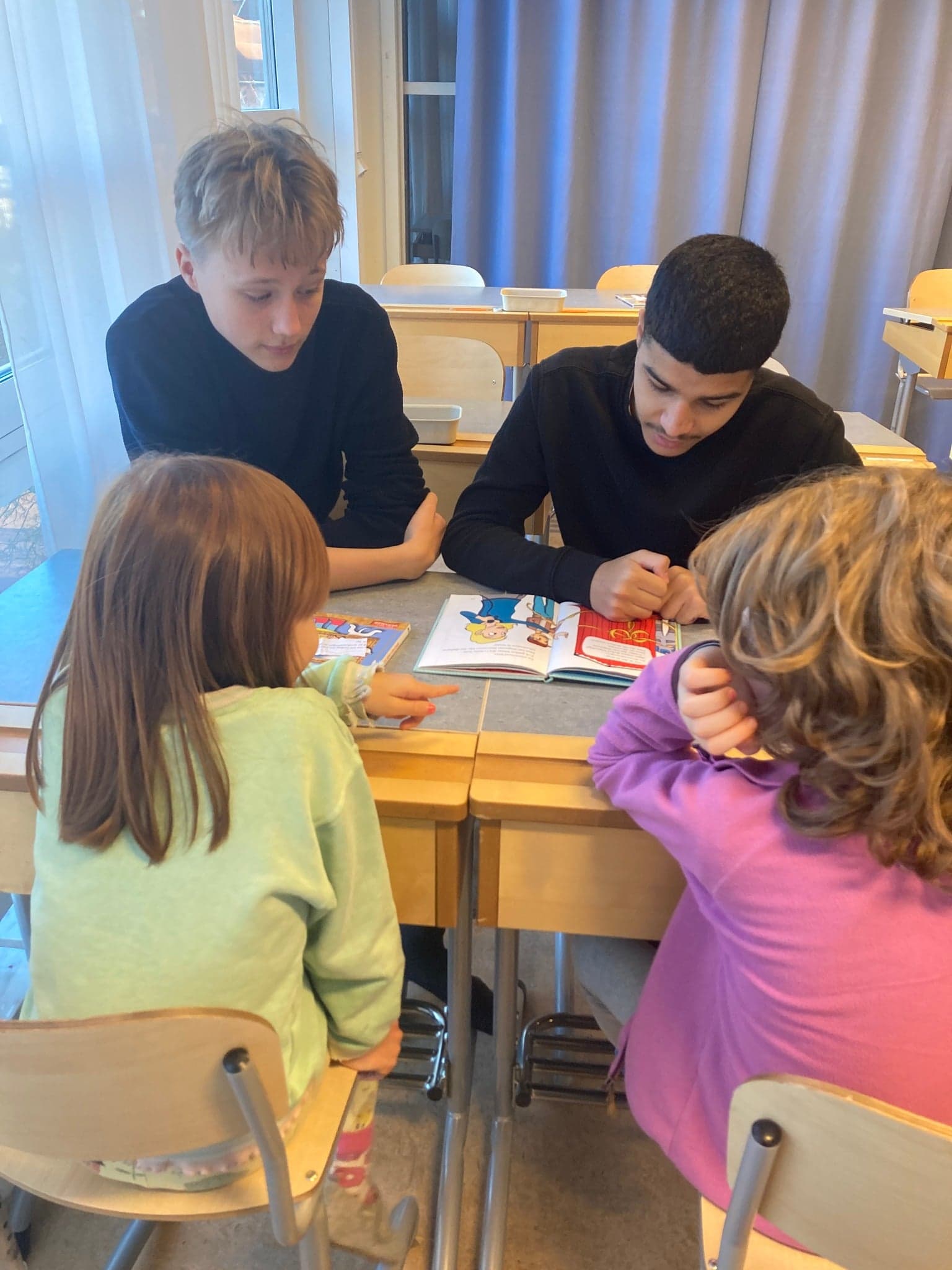 Äldre elev sitter på golvet och läser bok tillsammans med ett yngre fadderbarn.