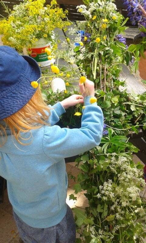 Ett förskolebarn i blå solhatt utforskar höga blommor i trädgården.