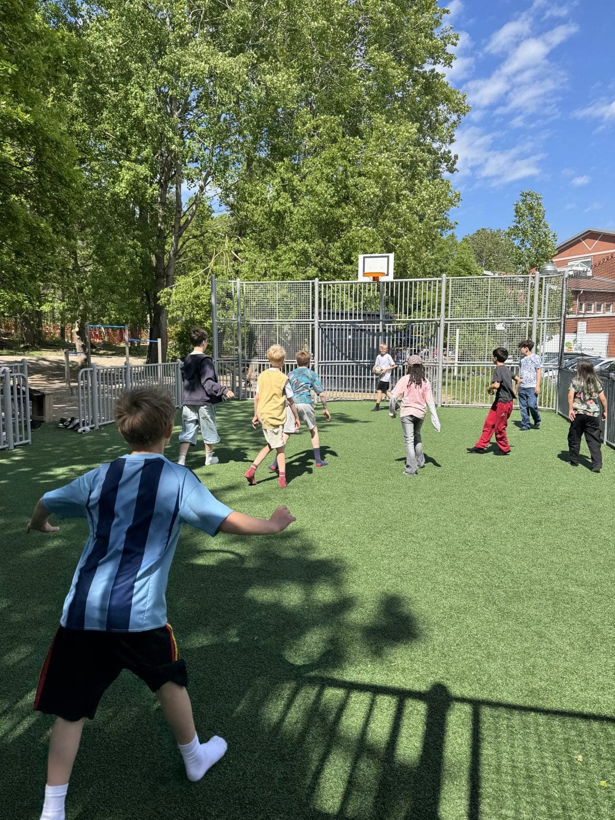 Elever spelar fotboll på skolans konstgräsplan en solig sommardag.
