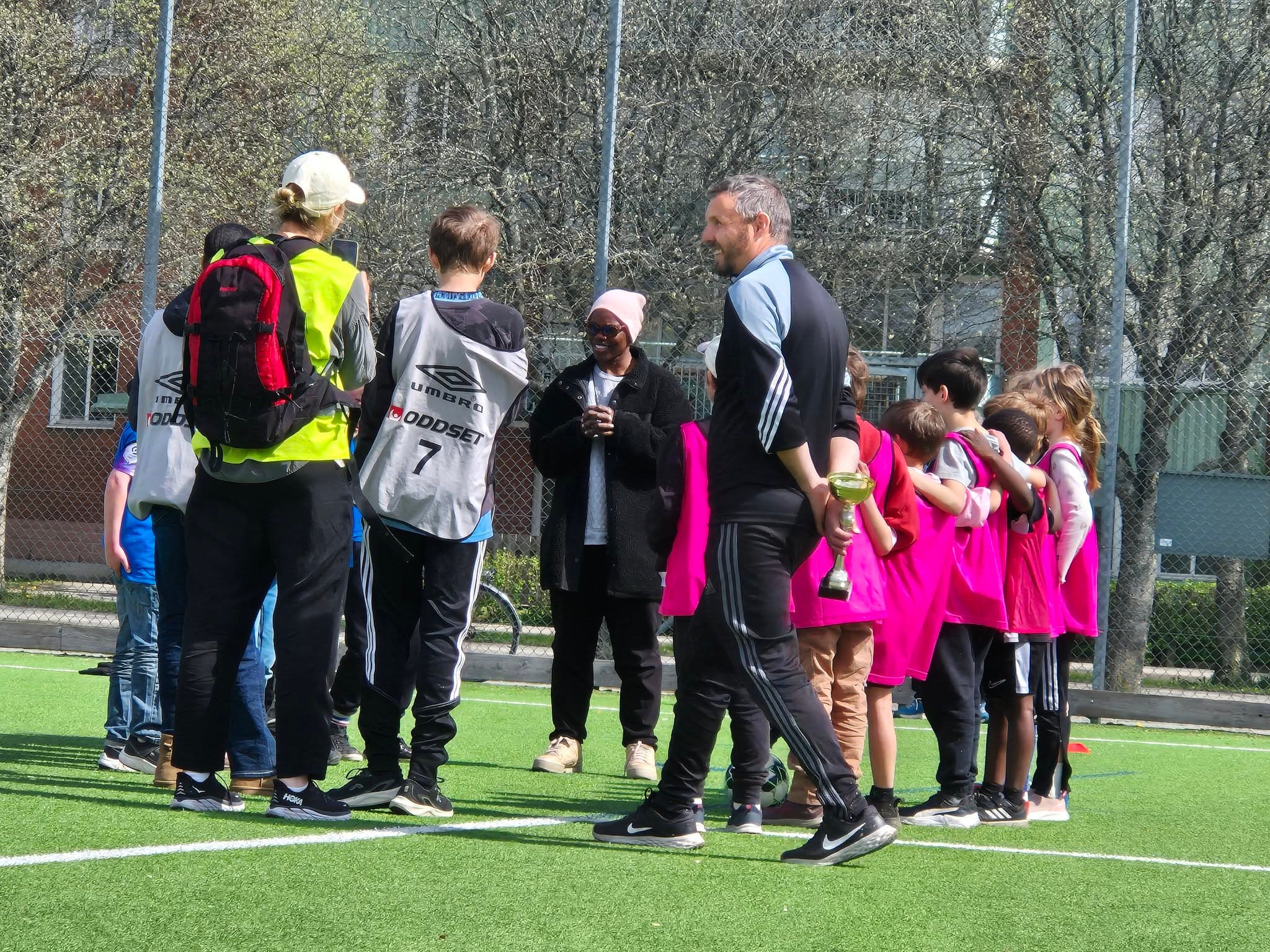 Elever på fotbollsplan med pokal och fotbollsvästar efter en turnering.