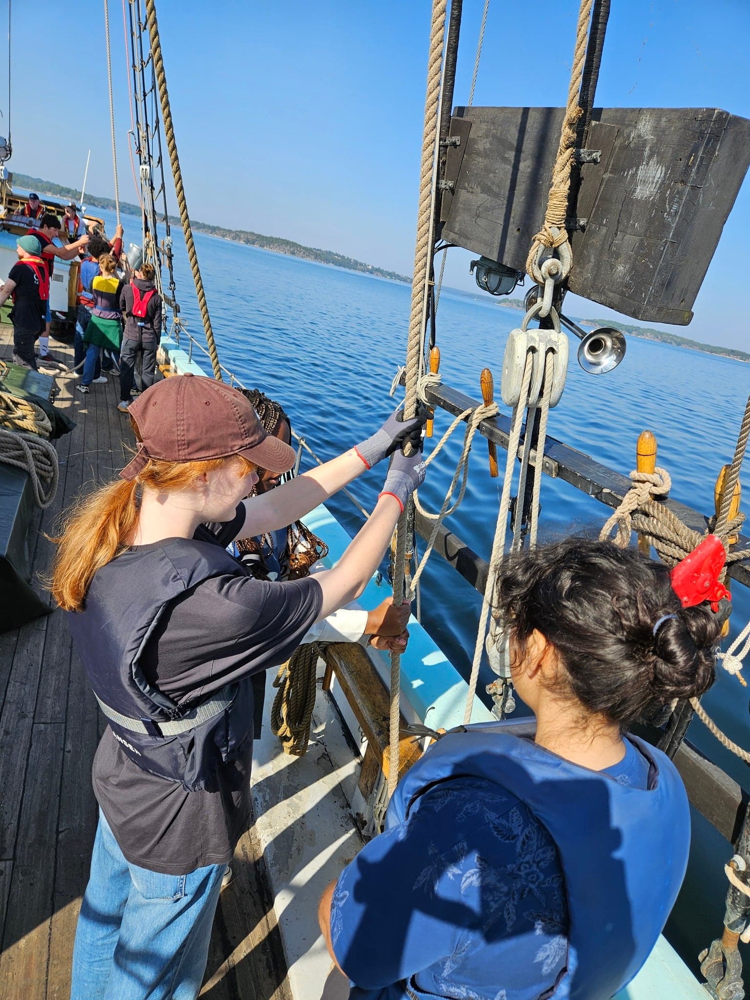Elever sköter rep och block ombord på en segelskuta ute på havet.