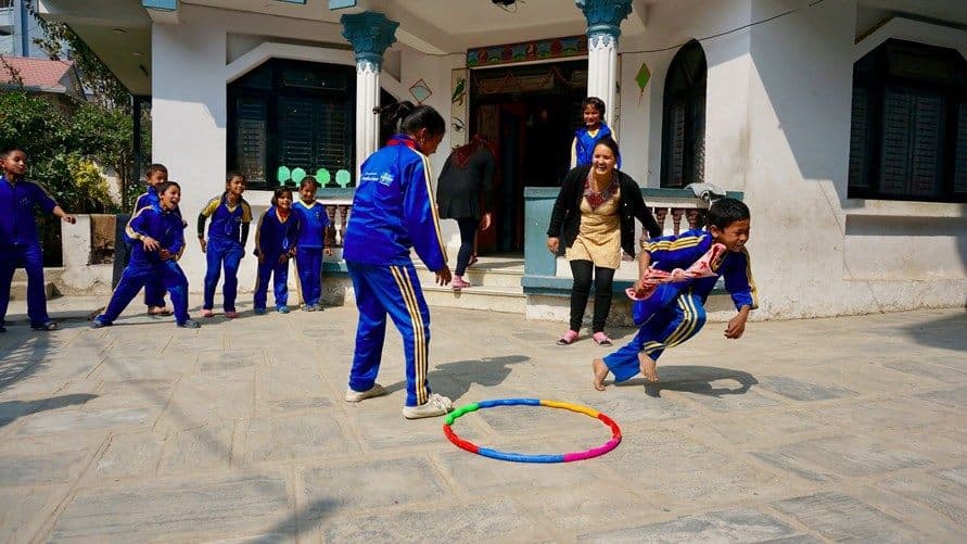 Elever leker med en färgglad rockring framför skolan i Nepal.