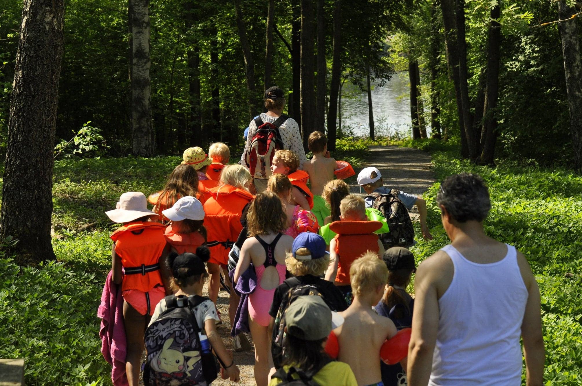 Barn i flytvästar på väg till simskola genom skogen.