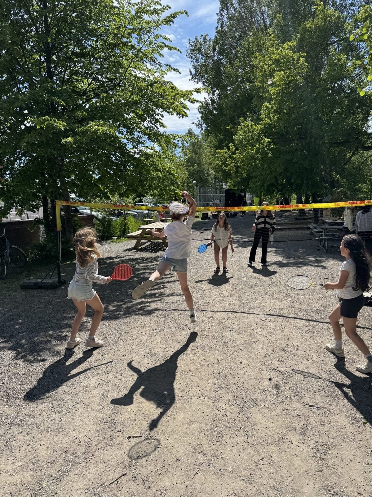 Elever spelar racketspel över ett uppspänt nät på skolgården en sommardag.
