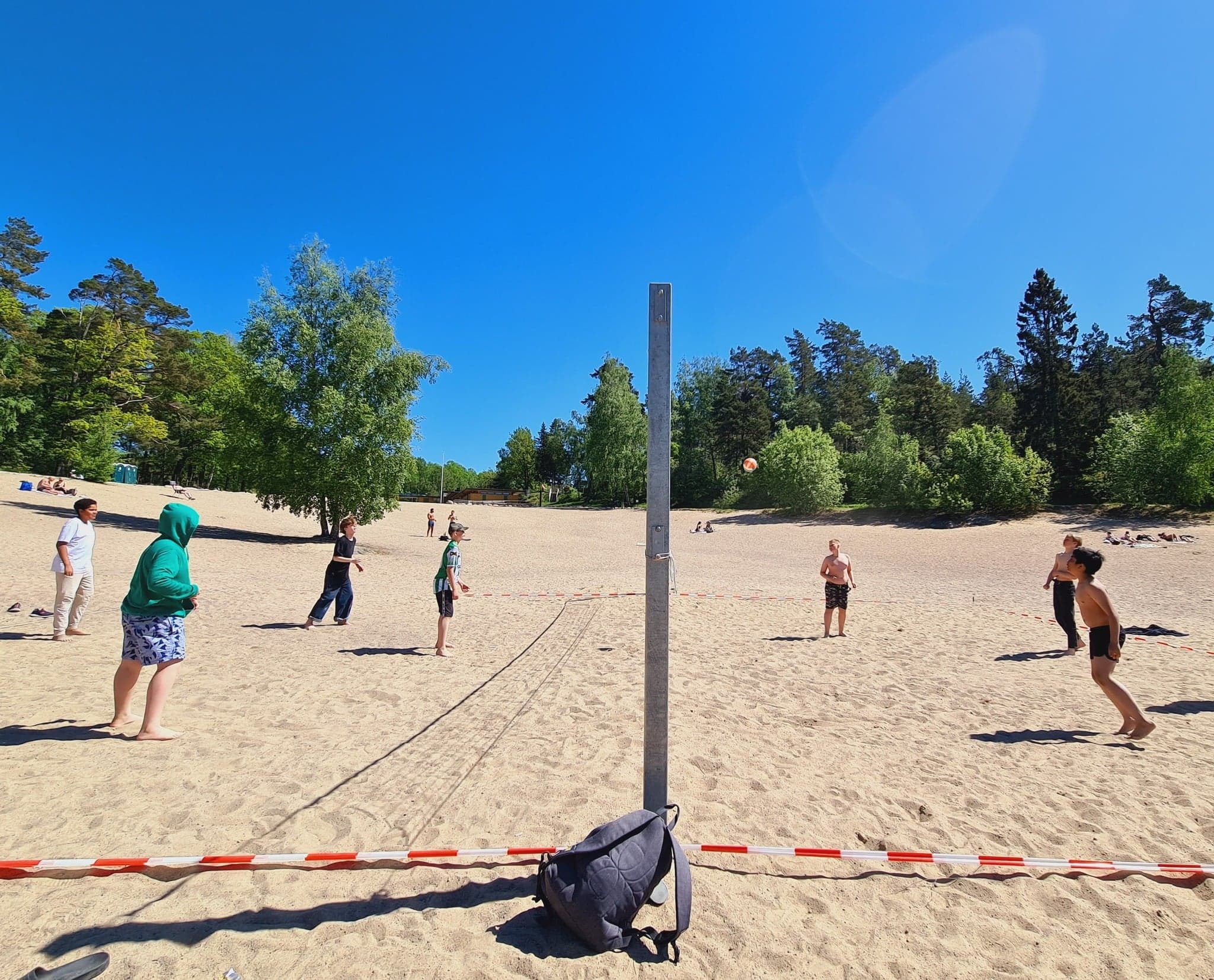 Äldre elever spelar volleyboll på en sandstrand en solig vårdag.